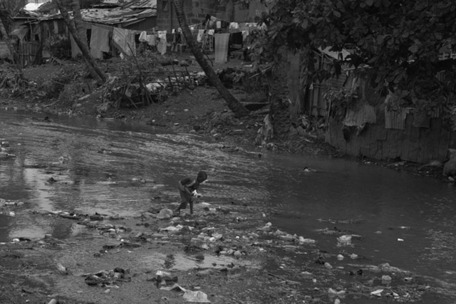 a young boy searches through floating trash in a river in a Freetown slum