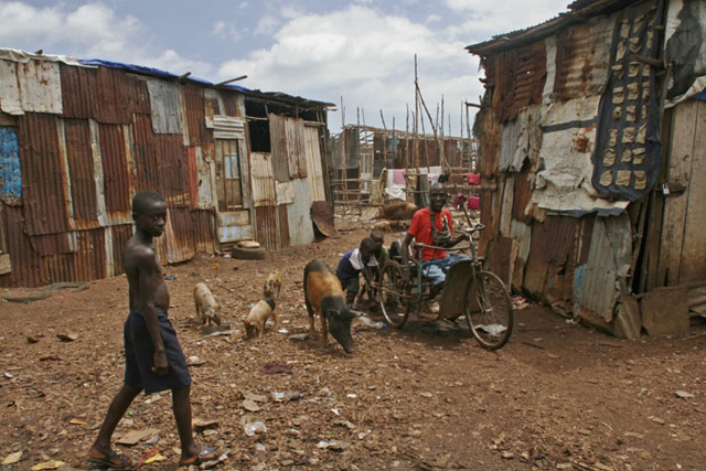 The man in the wheelchair being pushed by children, is a local teacher and aid worker. Photograph taken in  a Freetown slum. 